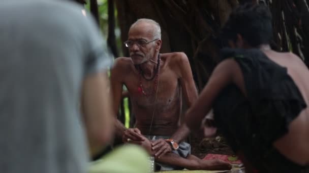 Arambol, Goa, Índia - Novomber 30, 2017: Baba indiano e seu amigo sentado sob a grande árvore baniana fazendo fogo e fumando maconha — Vídeo de Stock