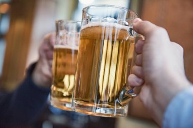 Birayla kadeh kaldıran iki adamın yakın çekimi.