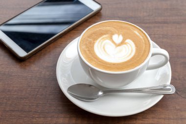Latte sanat ile smartphone ahşap arka plan üzerinde kahve fincanı 