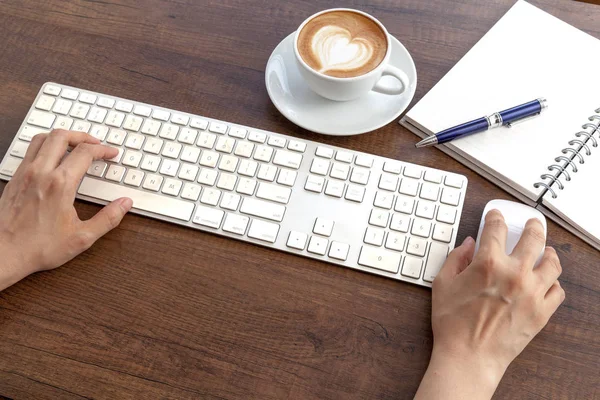 Typing and have a coffee cup of latte art heart shape on wooden