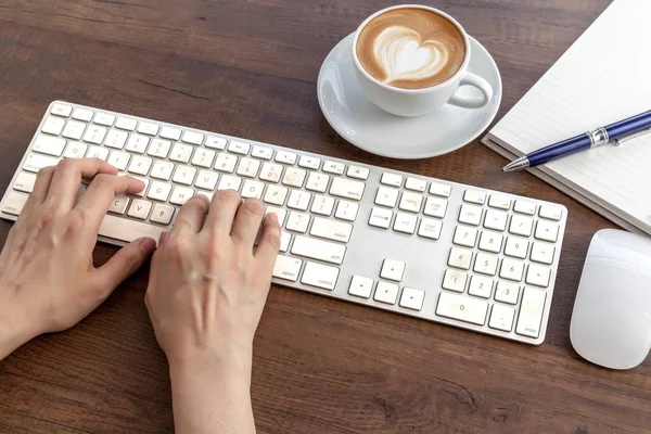 Typing and have a coffee cup of latte art heart shape on wooden