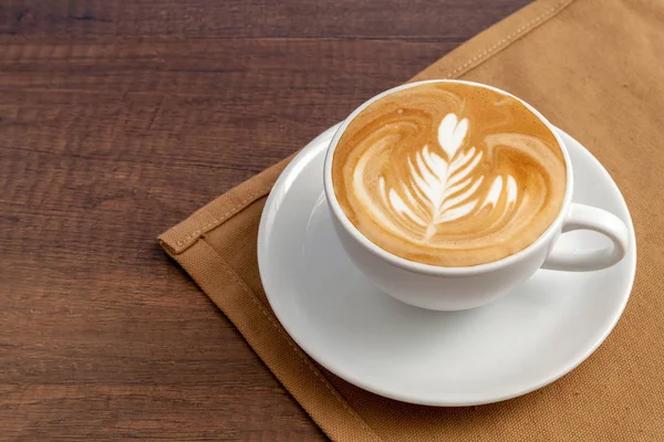 Xícara de café de roseta latte art place no guardanapo em fundo de madeira . — Fotografia de Stock