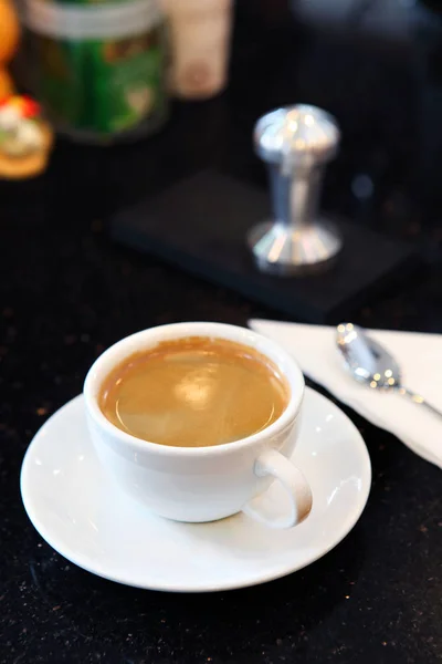 Caffè cremoso in tazza bianca su piatto con sfondo scuro — Foto Stock
