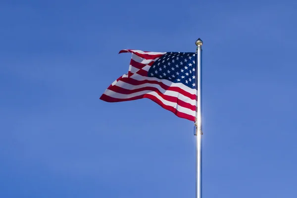 US flag flutters in the wind against the cloudless sky