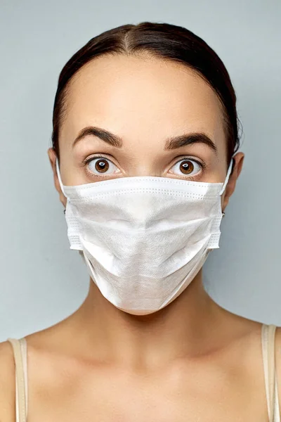 Brunette with brown eyes with a surprised look in a white disposable medical mask with fine hairdo — Stock Photo, Image