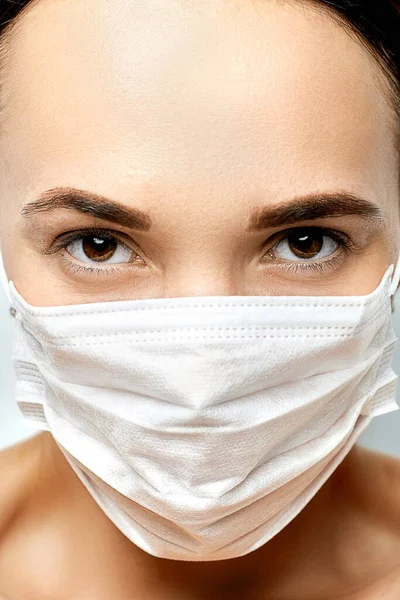 Young brunette with brown eyes in a white medical mask looks confidently — Stock Photo, Image