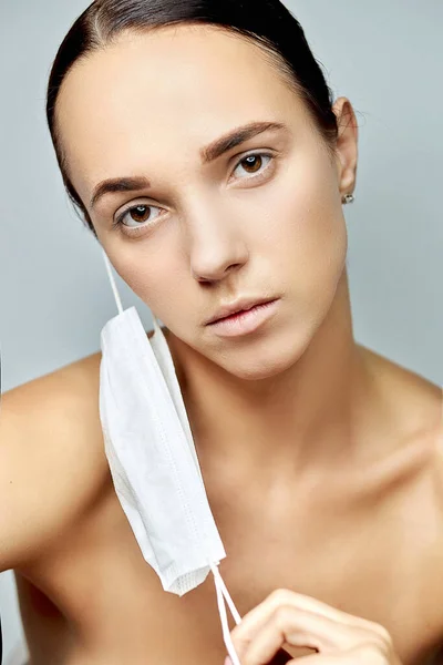 young brunette girl looking forward with a tired look with a flat white medical disposable mask on a long neck