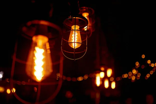 Accogliente, illuminazione lampada in un'istituzione su una parete di legno. lampadine di vetro appese al soffitto brillano e luce calda . — Foto Stock