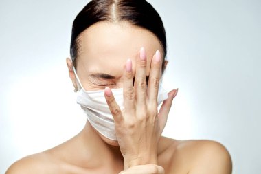 Yüzünde muhtemel koronavirüs belirtileri olan tıbbi maskeli bir kız yüzünü gri bir arka planda tutuyor.