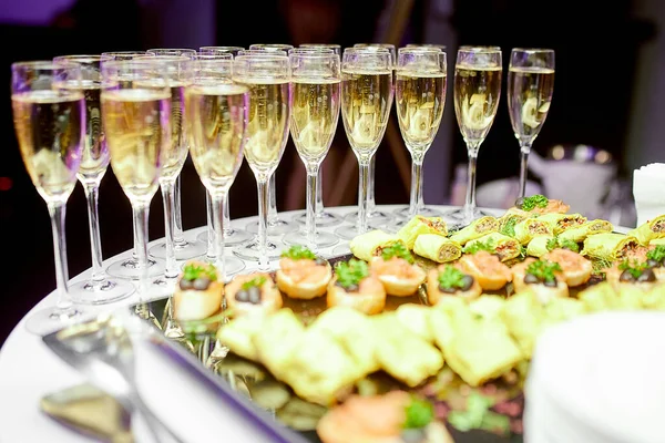 Copas de champán de cristal de pie en una mesa de servir y en frente de diferentes aperitivos para los huéspedes —  Fotos de Stock