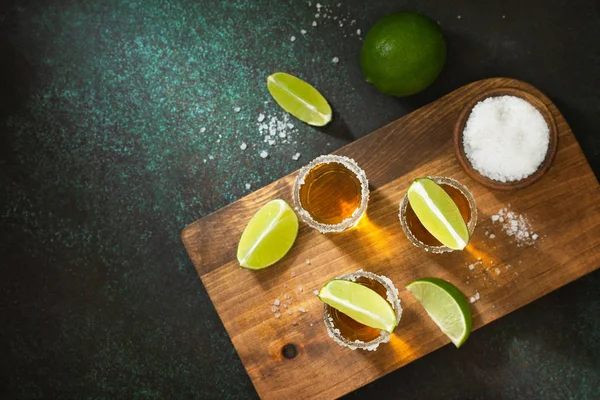 Tequila en or mexicain avec citron vert et sel sur fond de pierre sombre — Photo