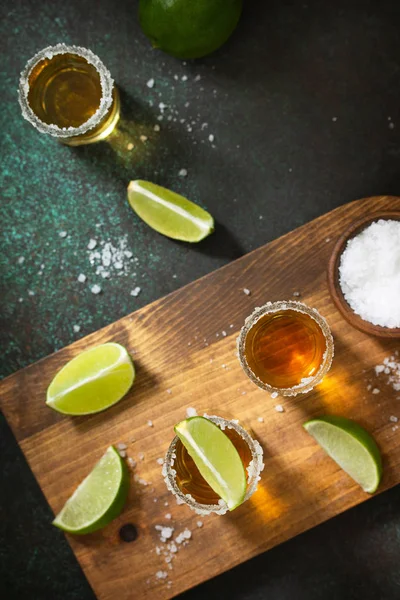 Tequila en or mexicain avec citron vert et sel sur fond de pierre sombre — Photo