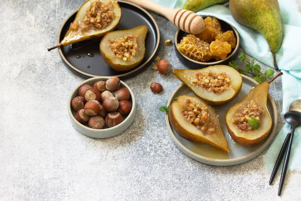 Healthy diet dessert. Baked pears with hazelnuts, honey and granola on a slate, stone or concrete background. Copy space.