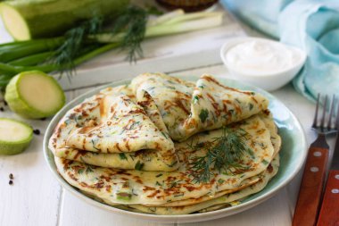 Atıştırmalık ya da yaz yemeği. Tahta bir masada ekşi kremayla servis edilen yeşil kabaklı gözleme..