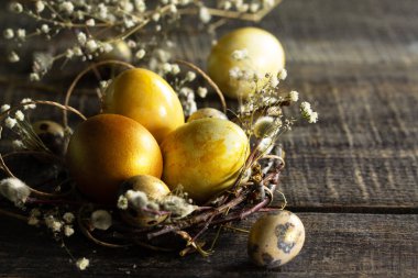 Paskalya yumurtaları. Yuvadaki altın paskalya yumurtaları ve tahta masanın üzerindeki paskalya süsleri. Boşluğu kopyala.