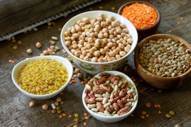 Diyet ve sağlıklı beslenme konsepti, vegan protein kaynağı. Tahta masa üzerinde çiğ baklagiller (nohut, kırmızı mercimek, Kanada mercimek, fasulye, bulgur). 