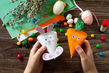 Çocuk paketleri havuç ve Paskalya Tavşanı şeklinde tutuyor. El yapımı. Çocukların yaratıcılığı projesi, el işleri, çocuklar için el sanatları..