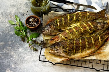 Pesto soslu fırında somon balığı ve gri bir tezgahta mutfak baharatları..