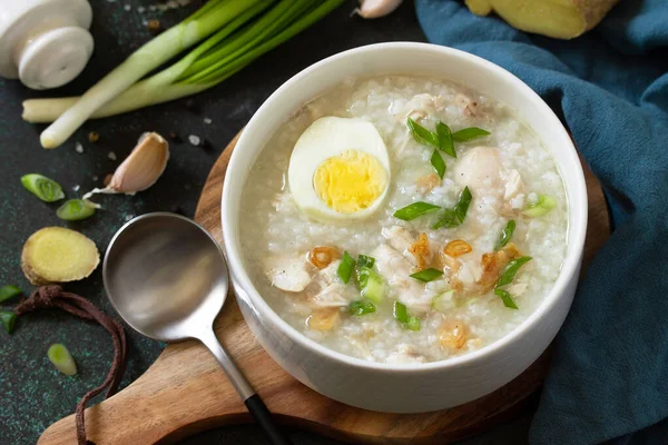 Arroz Caldo Soup. Hot soup with ginger chicken rice and garlic in a bowl on a dark countertop.