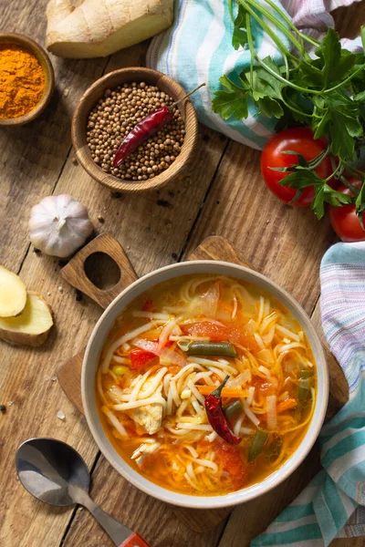 Tukpa soup of Indian cuisine. Hot noodle soup with chicken, ginger, cilantro and spices on a deyven wooden table. Top view flat lay background.