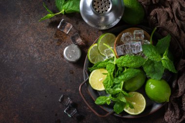 Mojito kokteyllerini tazeliyorum. Nane, kireç, buz malzemesi ve koyu taştan bir arka planda bar aletleri. Üst görünüm düz arkaplan. Boşluğu kopyala.