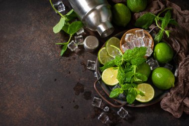 Mojito kokteyllerini tazeliyorum. Nane, kireç, buz malzemesi ve koyu taştan bir arka planda bar aletleri. Boşluğu kopyala.