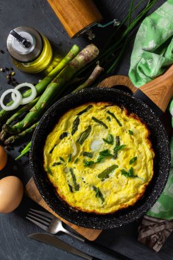 Sağlıklı kuşkonmaz omleti. Yumurtalı omlet, kuşkonmaz ve soğanlı taş bir tezgahın üstünde dökme demir tavada. Üst görünüm düz arkaplan.