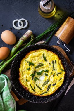 Sağlıklı kuşkonmaz omleti. Yumurtalı omlet, kuşkonmaz ve soğanlı taş bir tezgahın üstünde dökme demir tavada. Üst görünüm düz arkaplan.