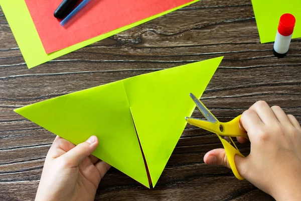Origami instruction step 5. Paper wind mill. Fun toy watermelon windmill spinning on a wooden table. Children\'s art project, needlework, crafts for children.