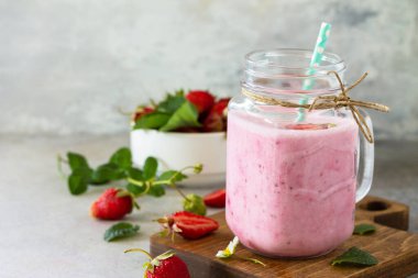 Doğal detoks, meyve tatlısı, sağlıklı beslenme konsepti. Çilekli yoğurtlu smoothie ya da cam kavanozdaki milkshake ya da taş levha üzerinde. Boşluğu kopyala.