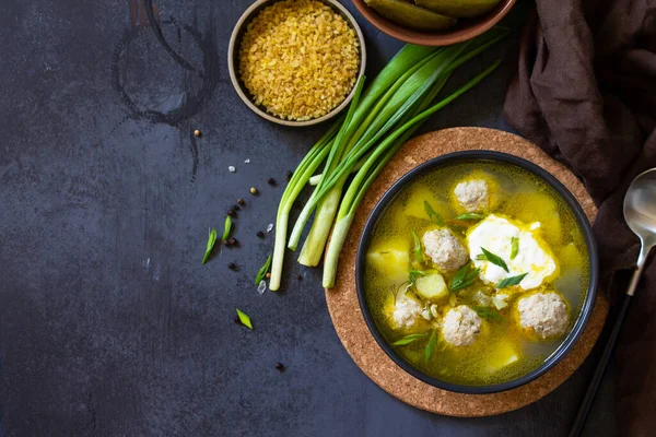 The concept of healthy and diet food. Russian or Ukrainian cuisine. Soup with meatballs, bulgur and pickled cucumbers on a dark stone table. Top view flat lay background. Copy space — Stock Image Concept Healthy Diet Food Russian Ukrainian Cuisine Soup Meatballs Bulgur Stock Picture