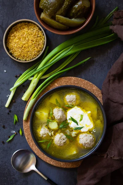 The concept of healthy and diet food. Russian or Ukrainian cuisine. Soup with meatballs, bulgur and pickled cucumbers on a dark stone table. Top view flat lay background. — Stock Image Concept Healthy Diet Food Russian Ukrainian Cuisine Soup Meatballs Bulgur Stock Photo