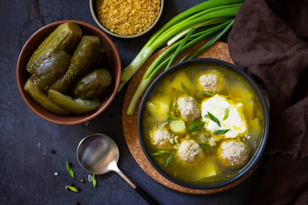 The concept of healthy and diet food. Russian or Ukrainian cuisine. Soup with meatballs, bulgur and pickled cucumbers on a dark stone table. — Stock Image Concept Healthy Diet Food Russian Ukrainian Cuisine Soup Meatballs Bulgur Stock Photo