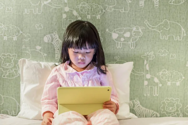 young little girl in pyjamas playing tablet on the bed