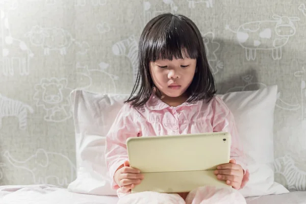 young little girl in pyjamas playing tablet on the bed