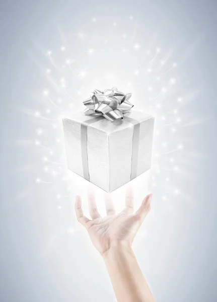 Hand met zilveren geschenk doos en magie twinkles — Stockfoto