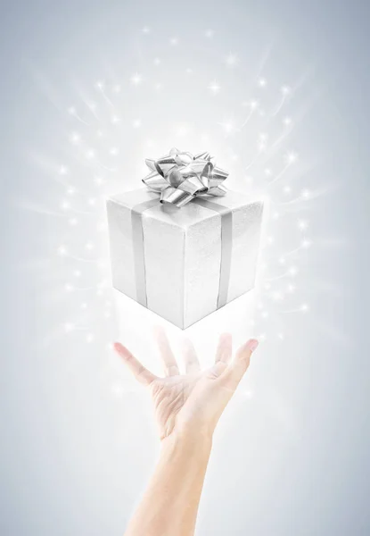hand with silver gift box and magic twinkles