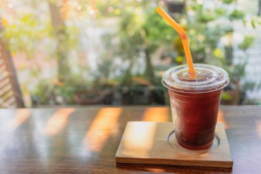 Plastik bardakta siyah kahve ve ahşap masada saman.