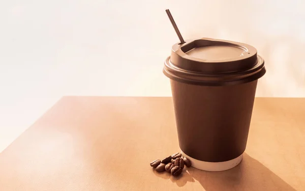 Papierowa filiżanka gorącej kawy, aby przejść ze słomką na szczycie drewnianego stołu w porannym słońcu — Zdjęcie stockowe