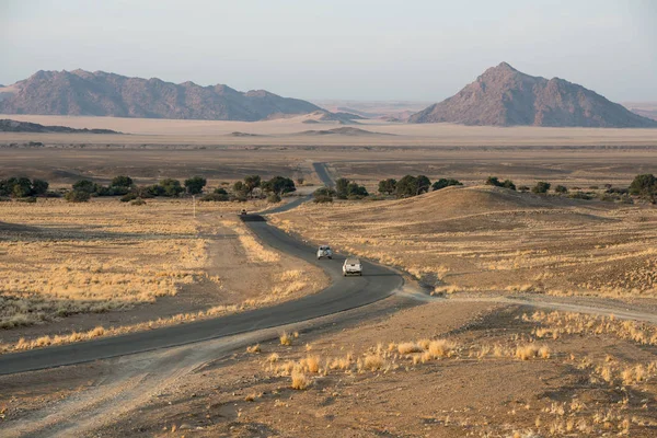 Modern asphalt road with cars is bending across Namibian fields — Stock Photo, Image