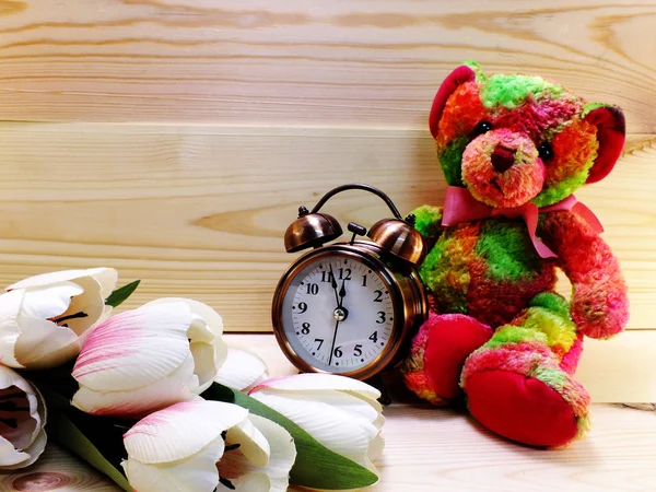 Tedy dragen met wekker en boeket bloemen op houten achtergrond — Stockfoto