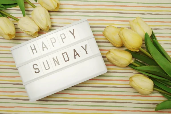 Happy Sunday Text in Light box flat lay with tulip flower bouquet