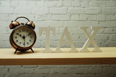 Ahşap zemin üzerinde alarm saati ve Vergi alfabesi harfi