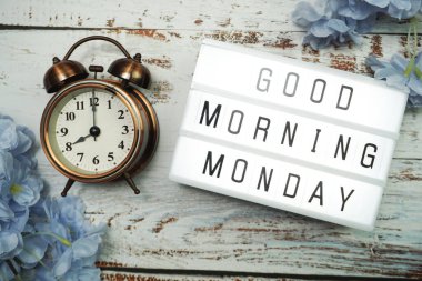 Günaydın pazartesi günü alarm saati ve ahşap arka planda çiçek desenli ışık kutusunda.