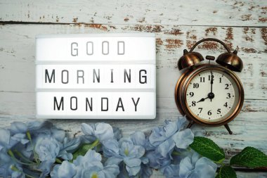 Günaydın pazartesi günü alarm saati ve ahşap arka planda çiçek desenli ışık kutusunda.