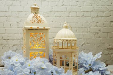 Beyaz tuğla duvar arka planında mum ışığı süslemesi olan beyaz metal fener