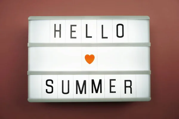 Hello Summer word in light box on white brick wall and wooden background