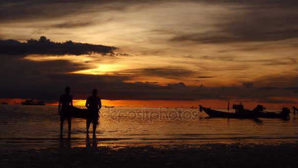 Wschód słońca na tropikalnej plaży. sylwetki łodzi i ludzi, piasek i morze. — Wideo stockowe