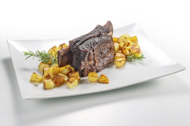 Dikdörtgen beyaz tabak pişmiş biftek kaburga ve kavrulmuş patates ile