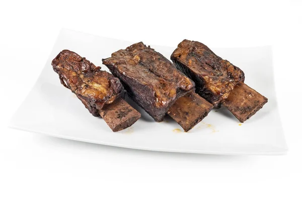 Vit rektangulär platta med tre kokta nötkött revben — Stockfoto